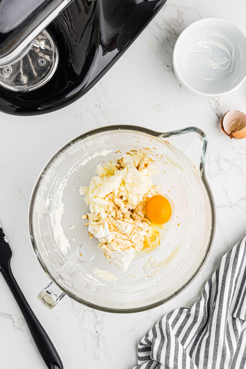 A mixing bowl with creamed butter and sugar, now with egg, vanilla extract, and sour cream added.