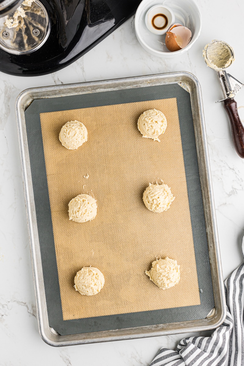 Portioned black and white cookie dough mounds neatly arranged on a parchment-lined baking sheet.