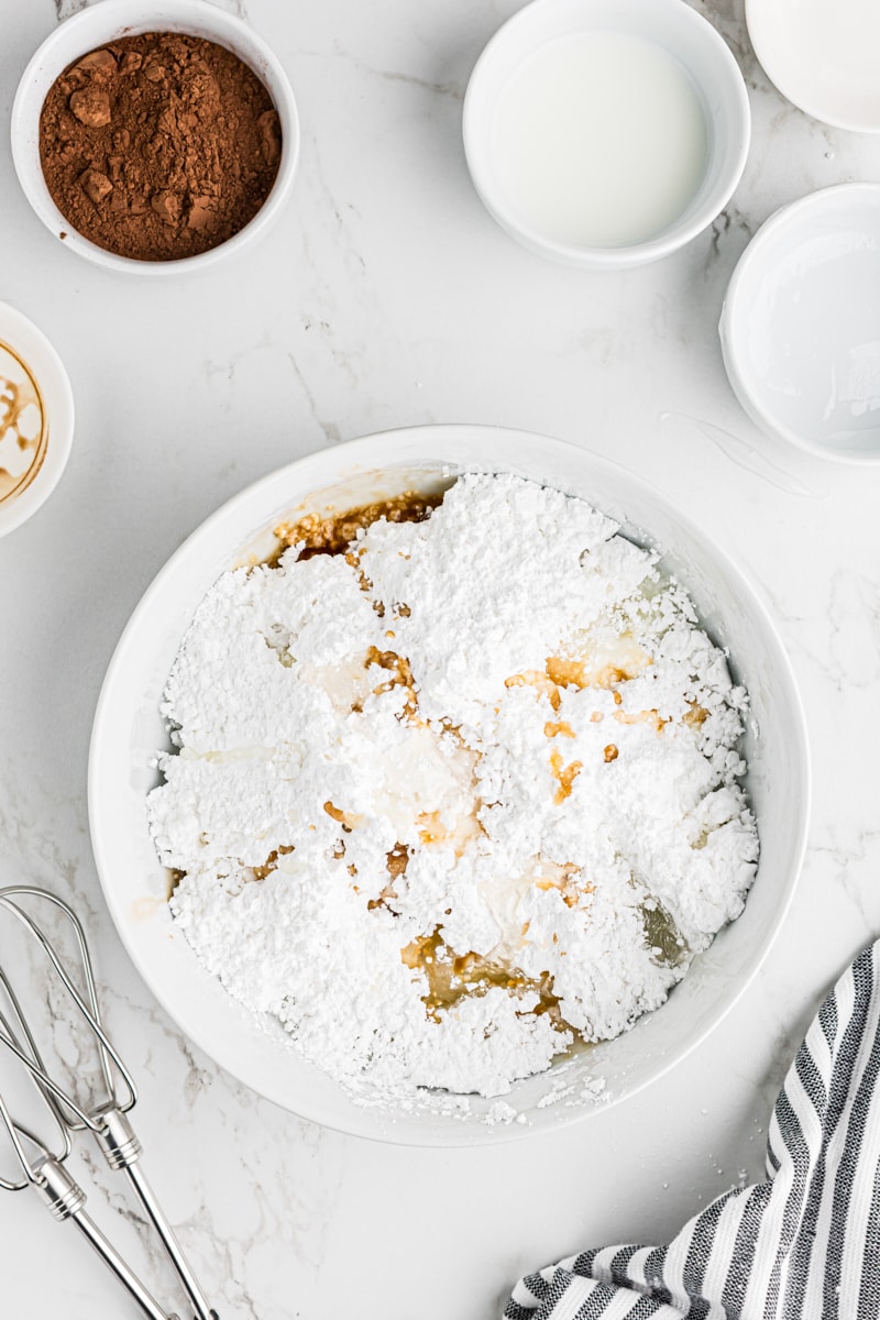 A white bowl containing confectioners’ sugar, milk, corn syrup, vanilla extract, and salt for the vanilla icing.