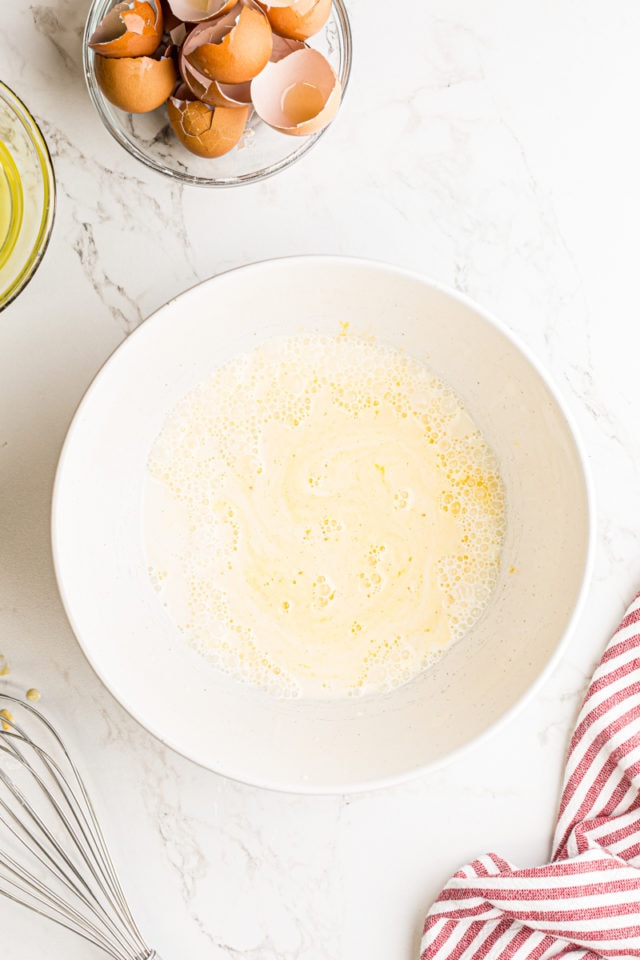 overhead view of milk, cream, and egg yolks in a white mixing bowl