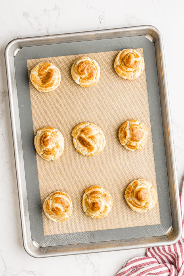 overhead view of freshly baked cream puffs on a baking sheet lined with a silicone baking mat