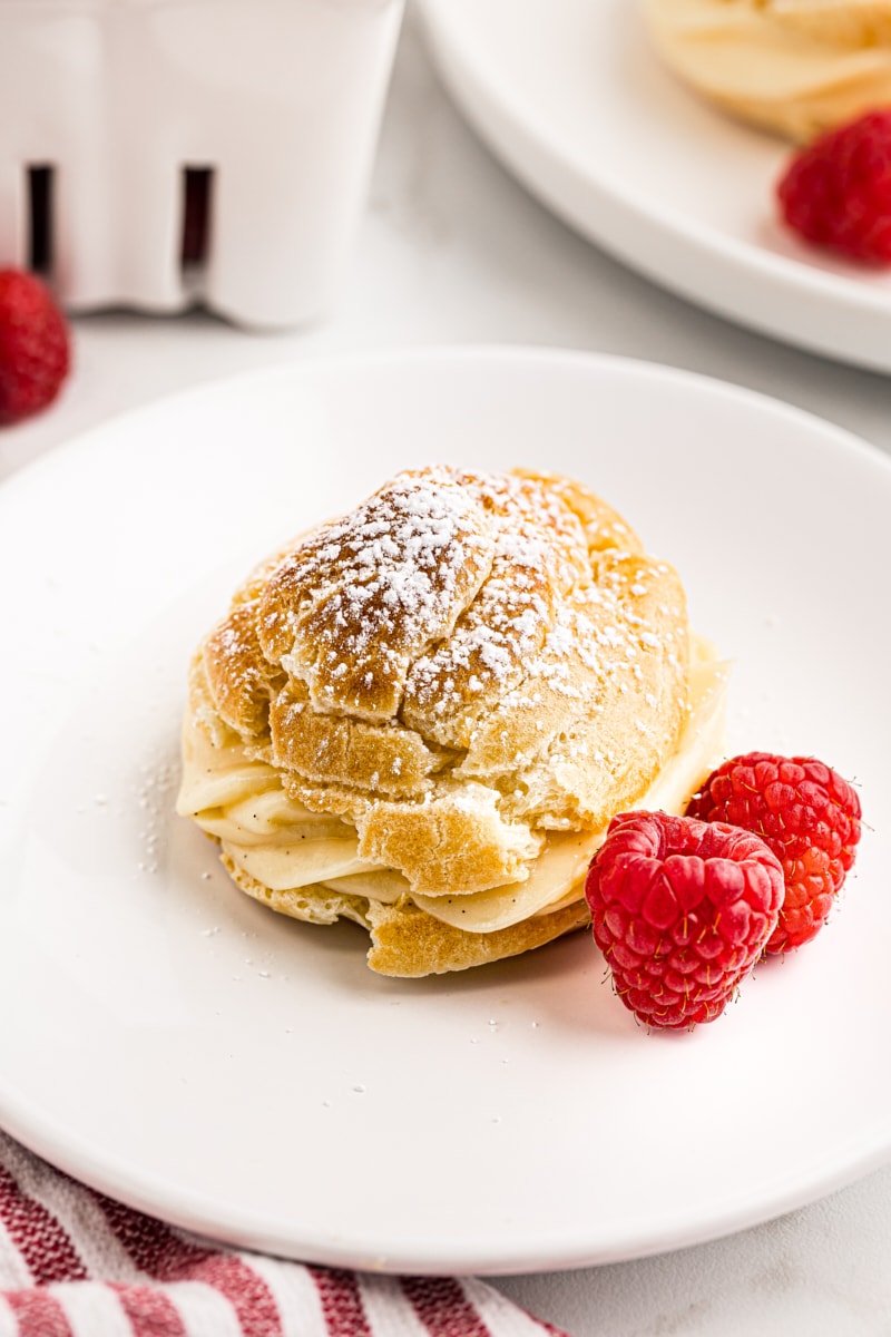 a cream puff and two raspberries on a white plate