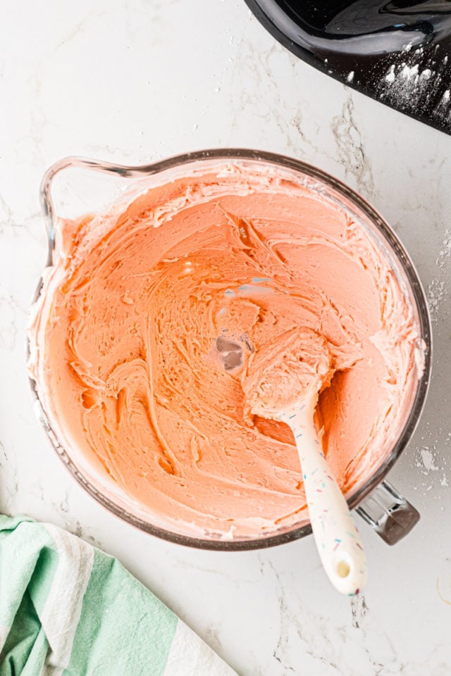 overhead view of pink frosting in a mixing bowl with a spatula