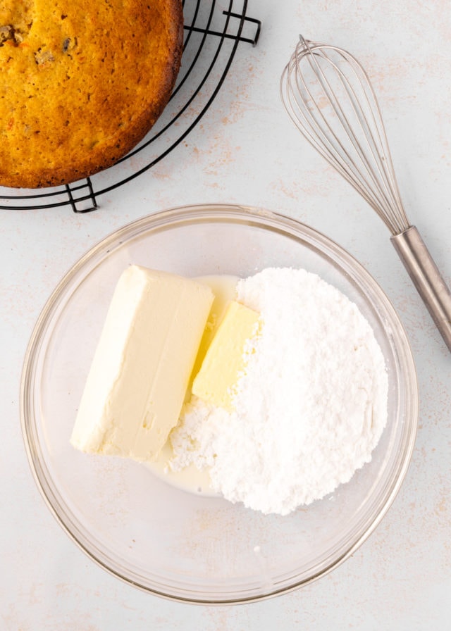 overhead view of cream cheese, butter, confectioners' sugar, and milk in a glass mixing bowl