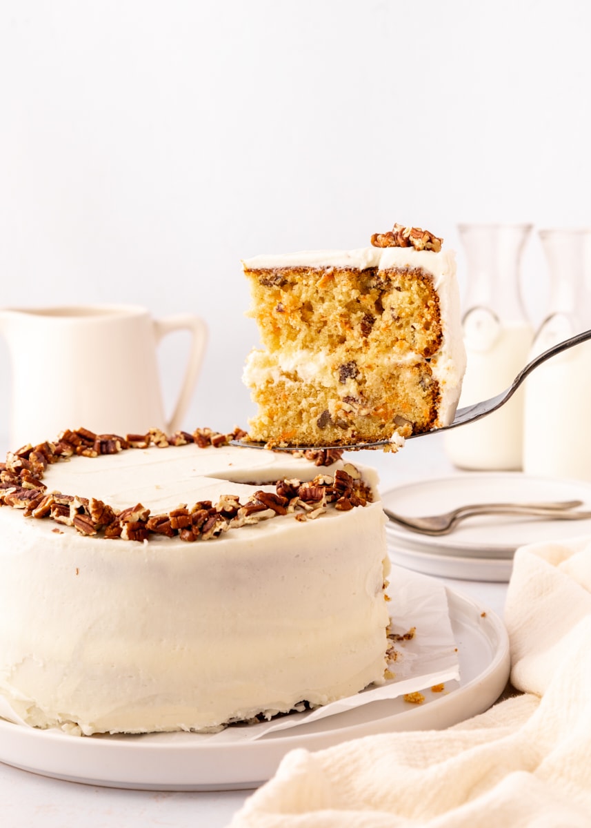 a slice of carrot cake on a cake server being lifted from the remaining cake