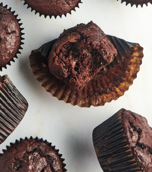 Overhead view of chocolate banana muffins on counter, with one muffin unwrapped and bitten