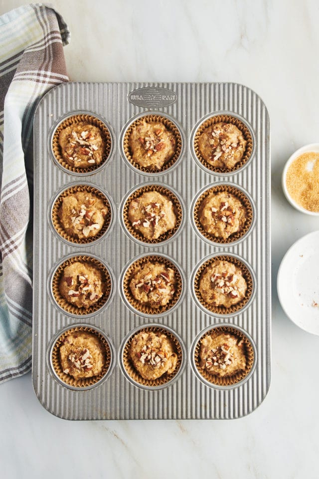Overhead view of cinnamon pecan muffin batter in pan topped with pecans