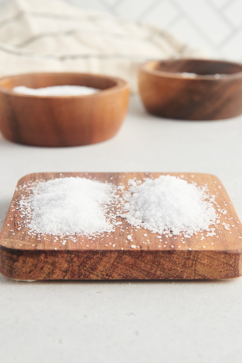 Morton kosher salt and Diamond Crystal kosher salt side by side on a small wooden board