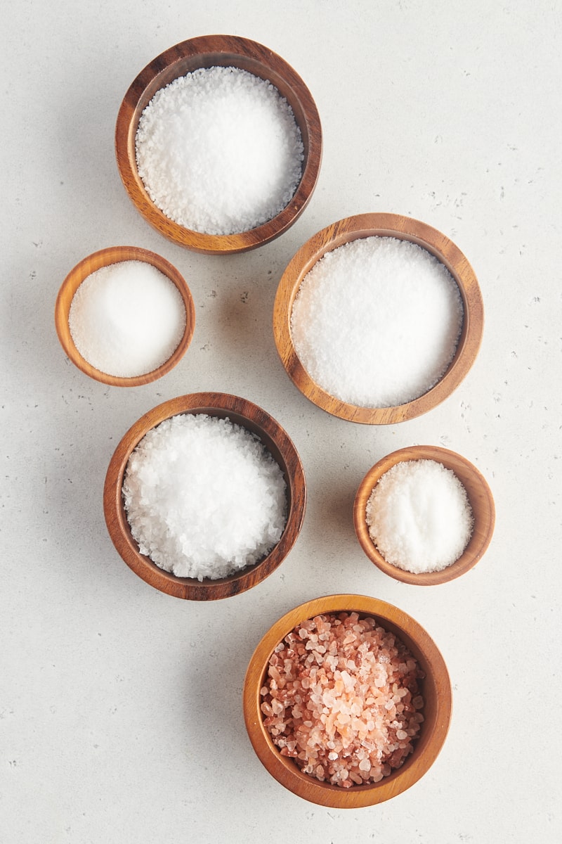 different types of salt in wooden bowls on a white surface