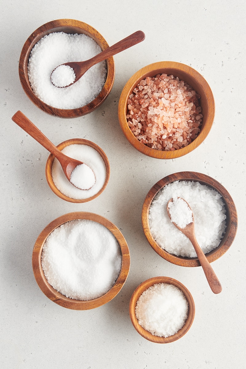 overhead view of table salt, kosher salt, sea salt, and Himalayan pink salt in small wooden bowls
