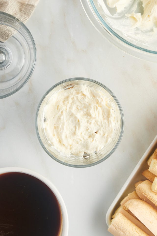 overhead view of mascarpone filling spread over ladyfingers in an individual glass serving bowl