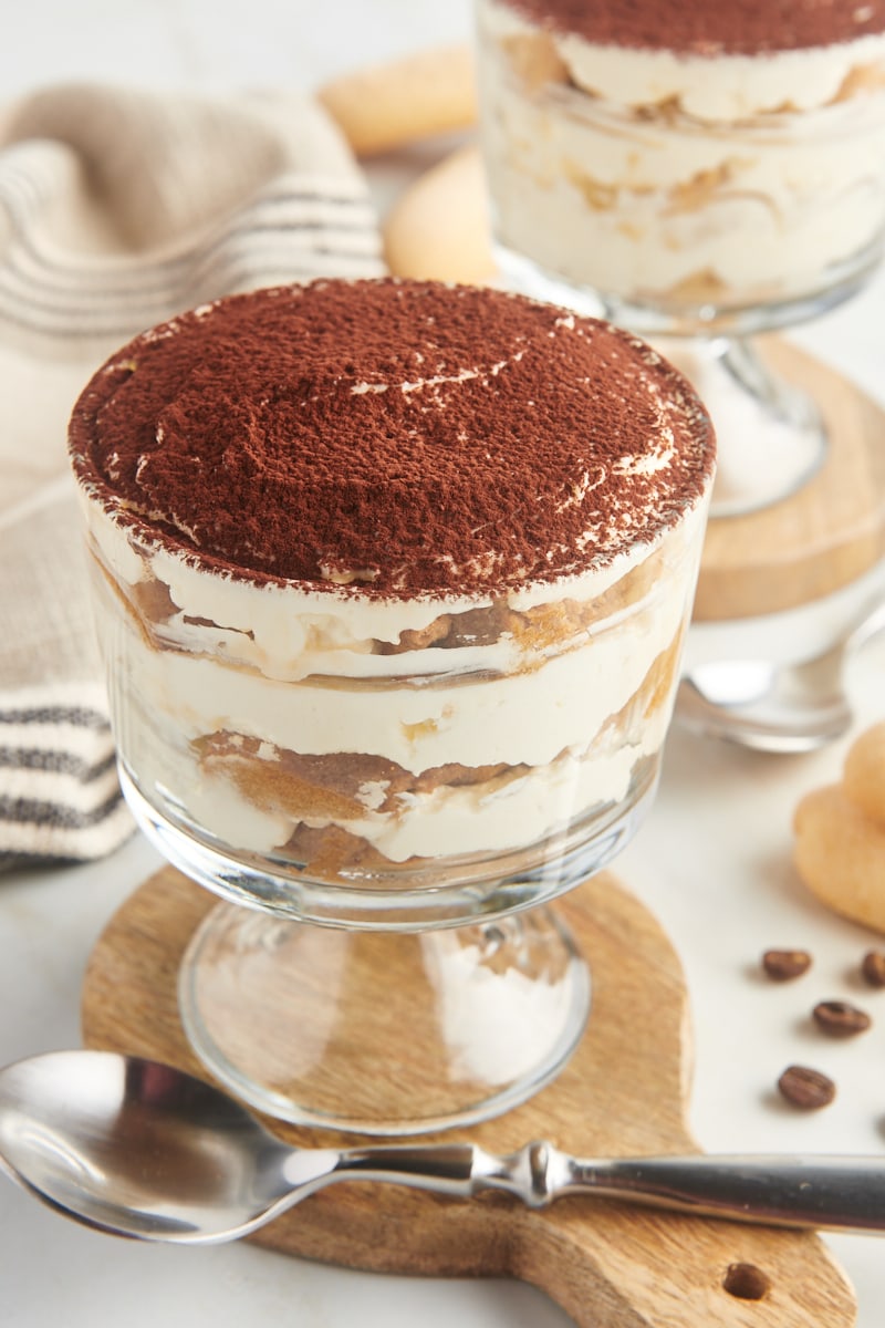 a serving of tiramisu for two in a glass footed bowl with the other serving in the background