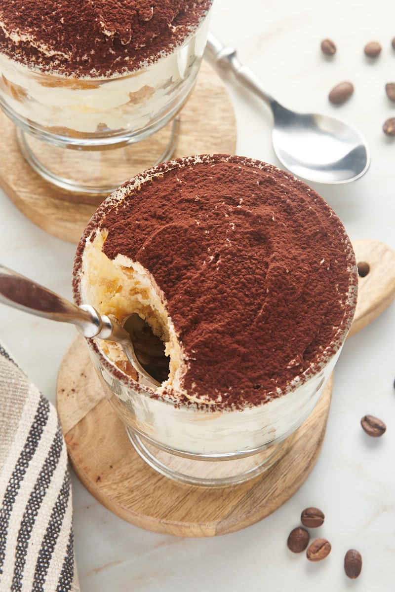 a spoon sticking down into a bowl of tiramisu where a bite is missing