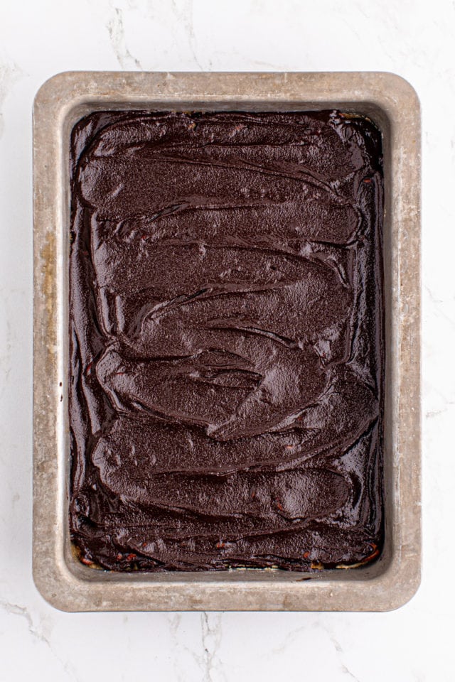 overhead view of ganache spread on top of butter pecan turtle bars in a rectangular baking pan