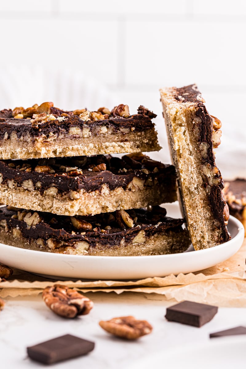 a stack of three butter pecan turtle bars with another propped against the stack on a white plate