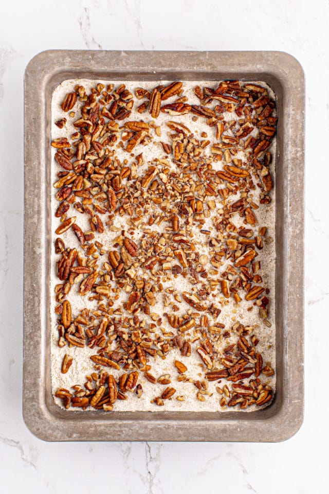 overhead view of pecans scattered over a shortbread crust in a rectangular baking pan