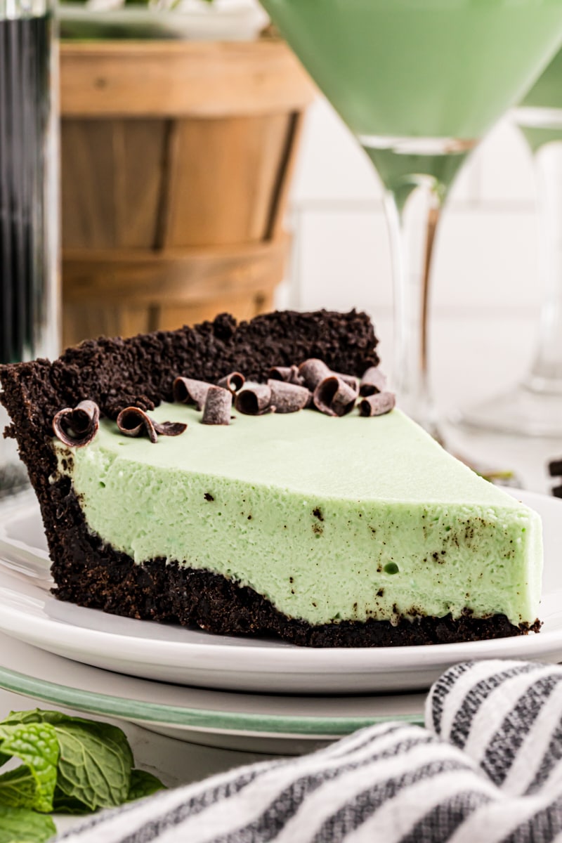 a slice of grasshopper pie on a white plate with a grasshopper cocktail in the background