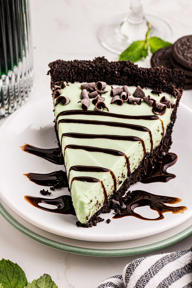 a slice of grasshopper pie on a white plate topped with chocolate curls and chocolate syrup