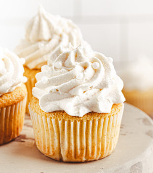 a vanilla cupcake on a wooden cake stand with more cupcakes behind