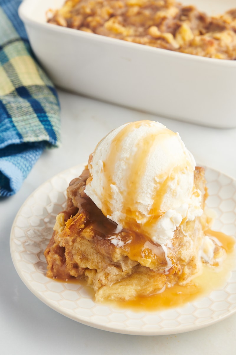 Piece of banana bread pudding on plate with ice cream and caramel on top