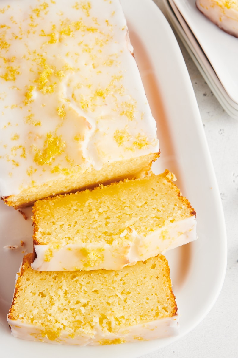 Overhead view of lemon loaf cake on platter with 2 slices cut