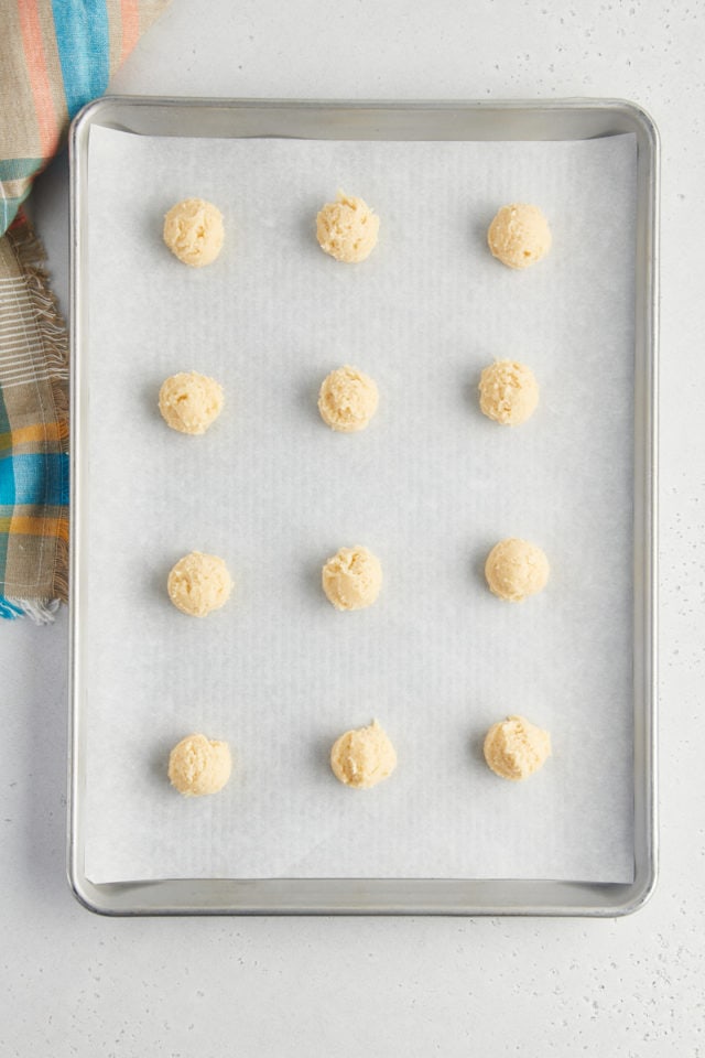 overhead view of sour cream cookie dough scooped onto a baking sheet lined with parchment paper
