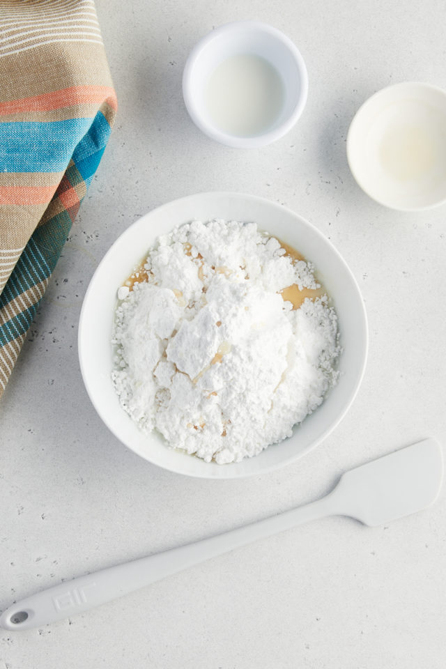 overhead view of confectioners' sugar, vanilla extract, and milk in a white mixing bowl