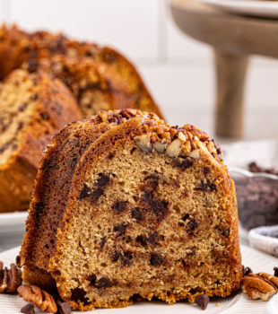 a slice of chocolate chip Bundt cake on a white plate with more cake in the background