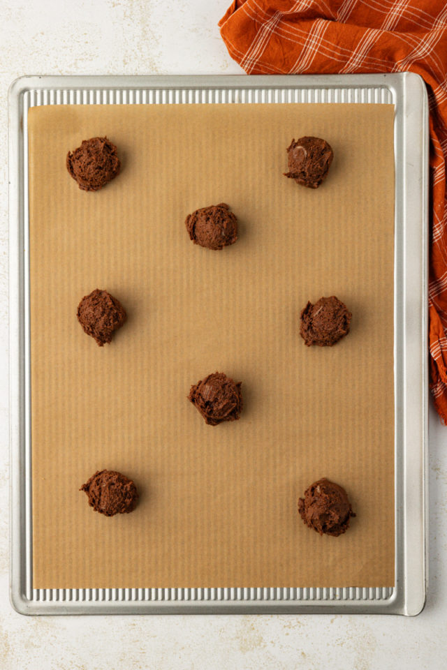 chocolate peanut butter cookie dough portioned into balls on a parchment-lined baking sheet