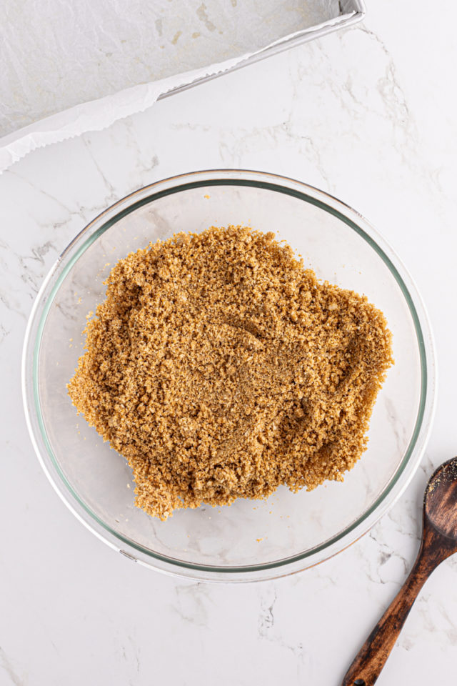 overhead view of mixed graham cracker crust mixture in a glass mixing bowl