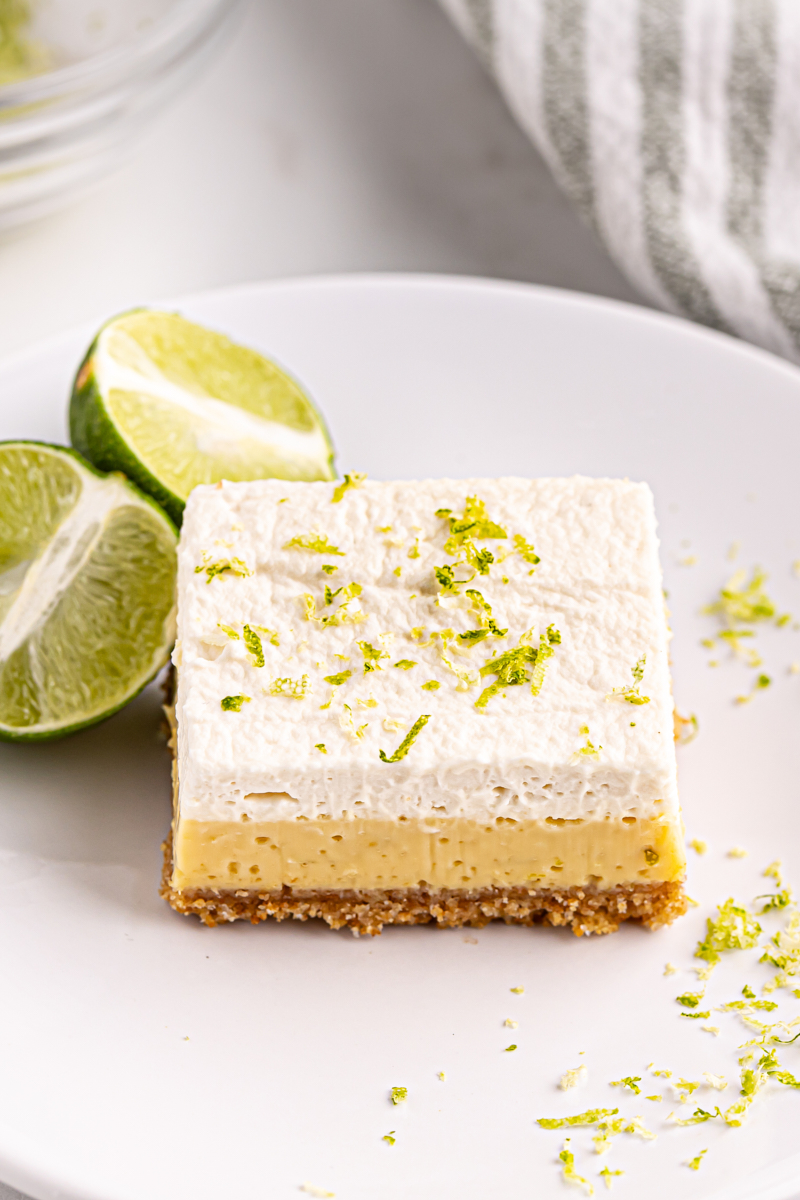 a key lime pie bar on a white plate with lime wedges