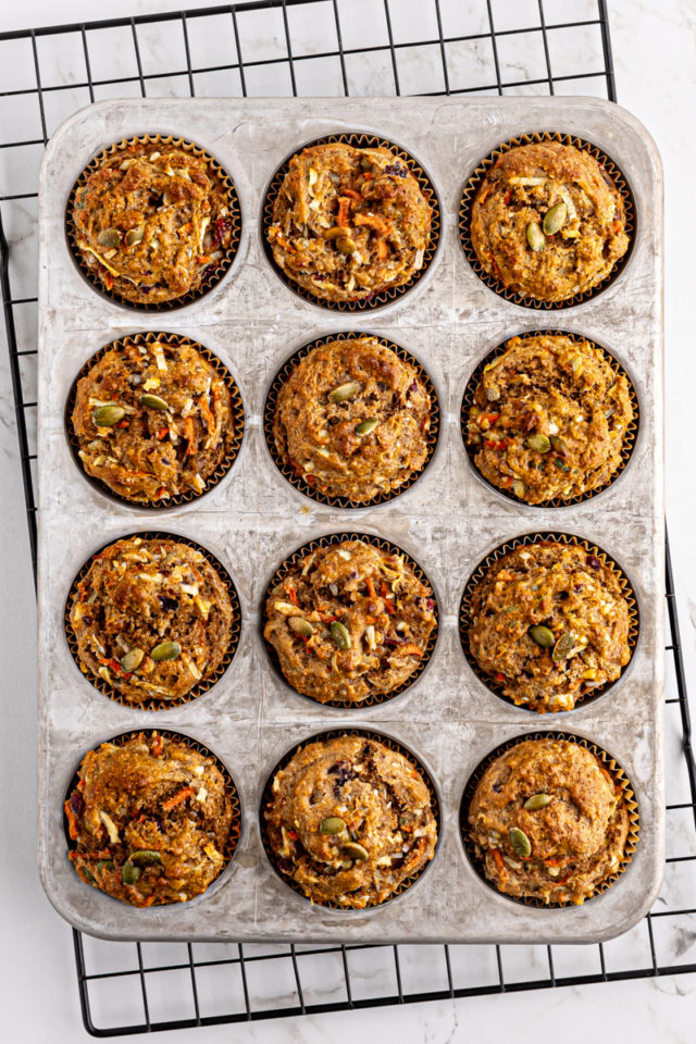 overhead view of freshly baked morning glory muffins in a muffin pan on a wire rack