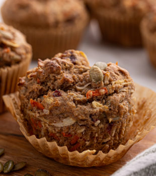 a partially unwrapped morning glory muffin with more muffins in the background