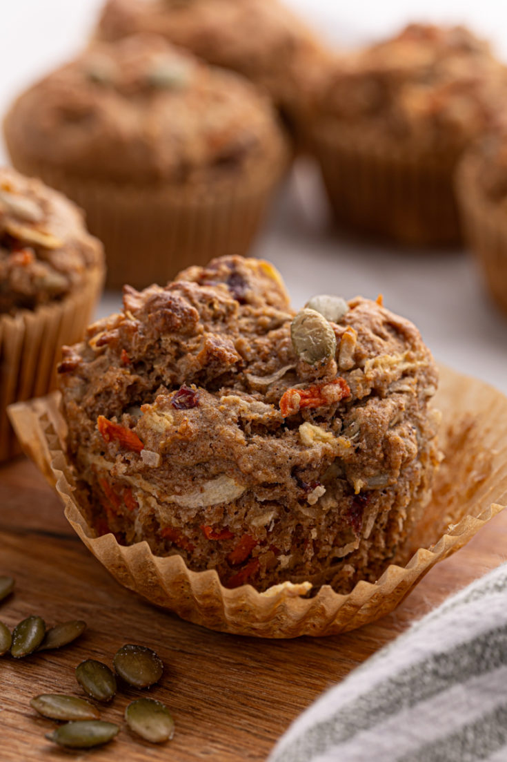 a partially unwrapped morning glory muffin with more muffins in the background