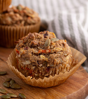 an unwrapped morning glory muffin on a wooden board with another muffin in the background
