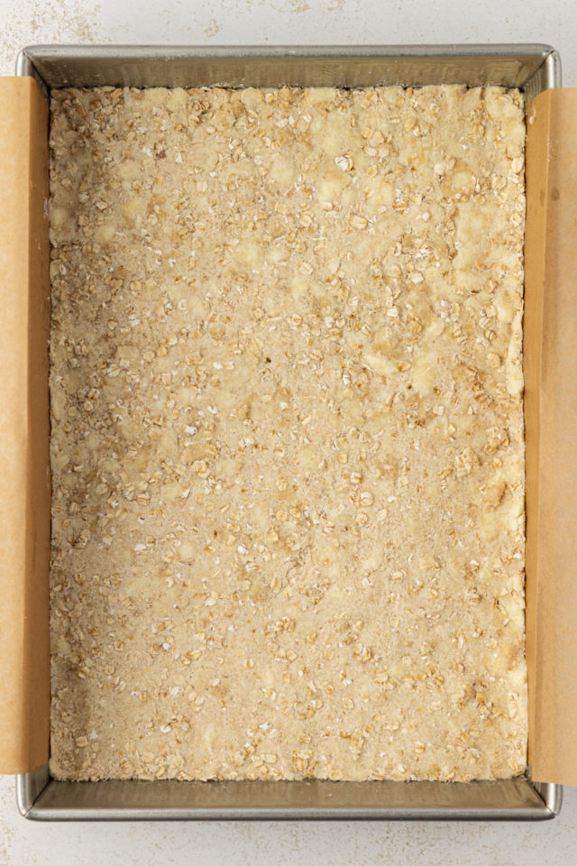 overhead view of raspberry oatmeal bars crust in a parchment-lined baking pan