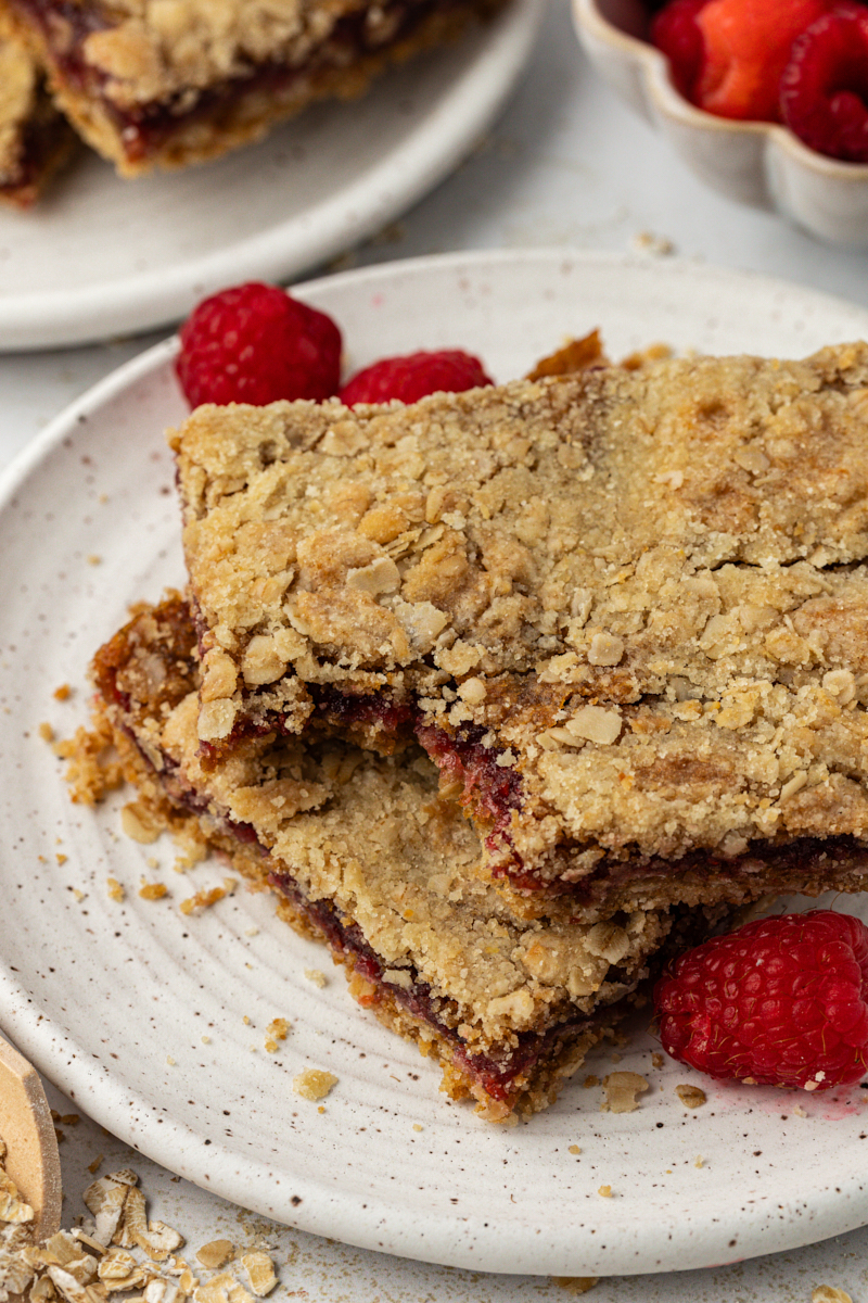a raspberry oatmeal bar with a bite missing stacked on top of another bar on a white plate