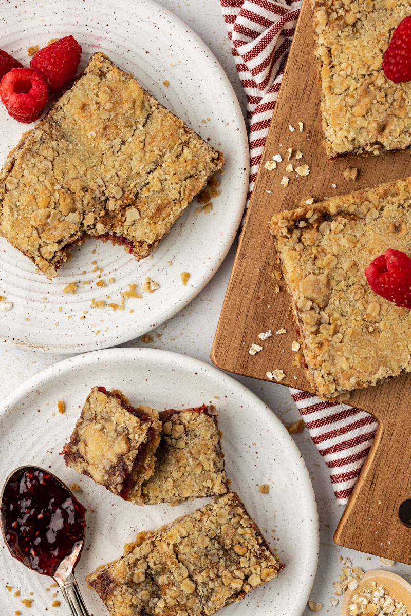 overhead view of raspberry oatmeal bars on white plates and a wooden cutting board