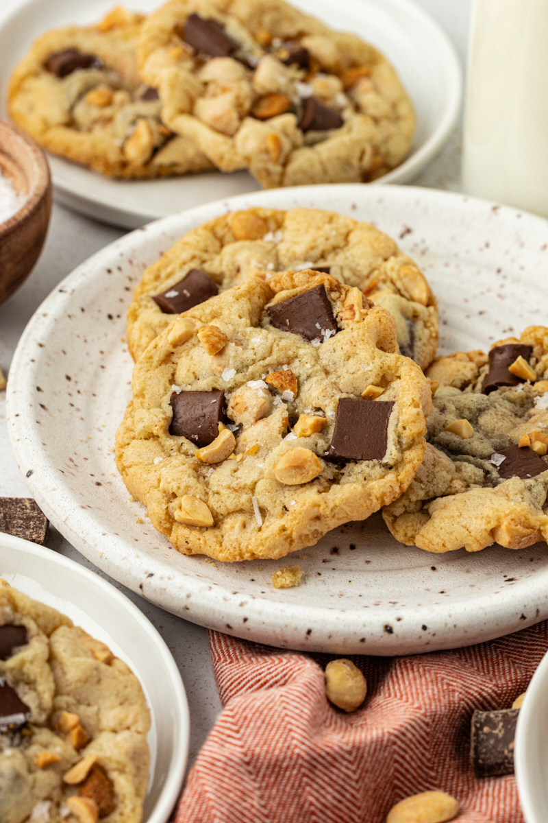 peanut chocolate chunk cookies on a brown-speckled white plate with more cookies alongside