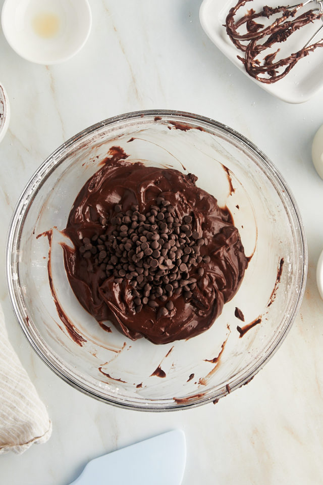 overhead view of chocolate chips added to brownie batter dip in a glass bowl