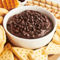 a bowl of brownie batter dip surrounded by various dippers on a wooden board