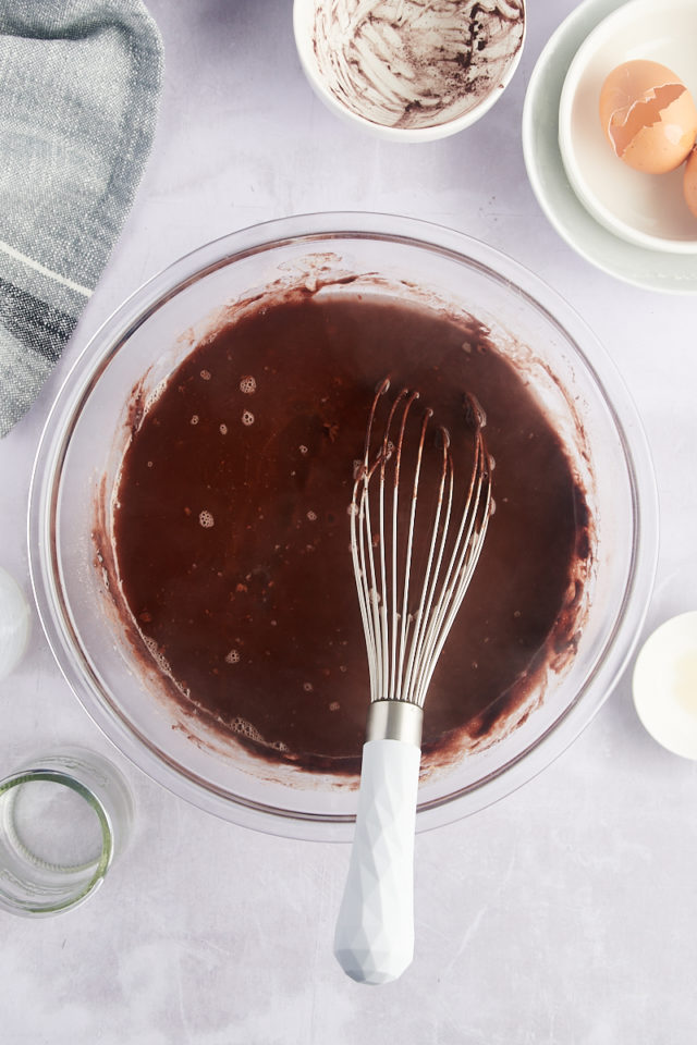 Overhead view of chocolate cake batter in bowl with whisk