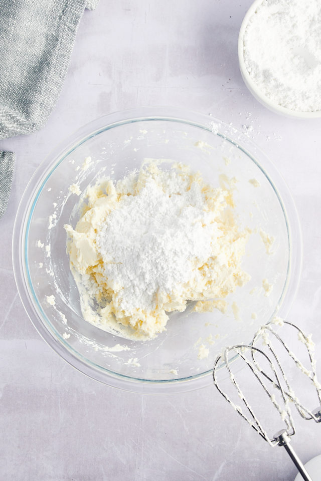 Overhead view of powdered sugar added to cream cheese mixture in bowl