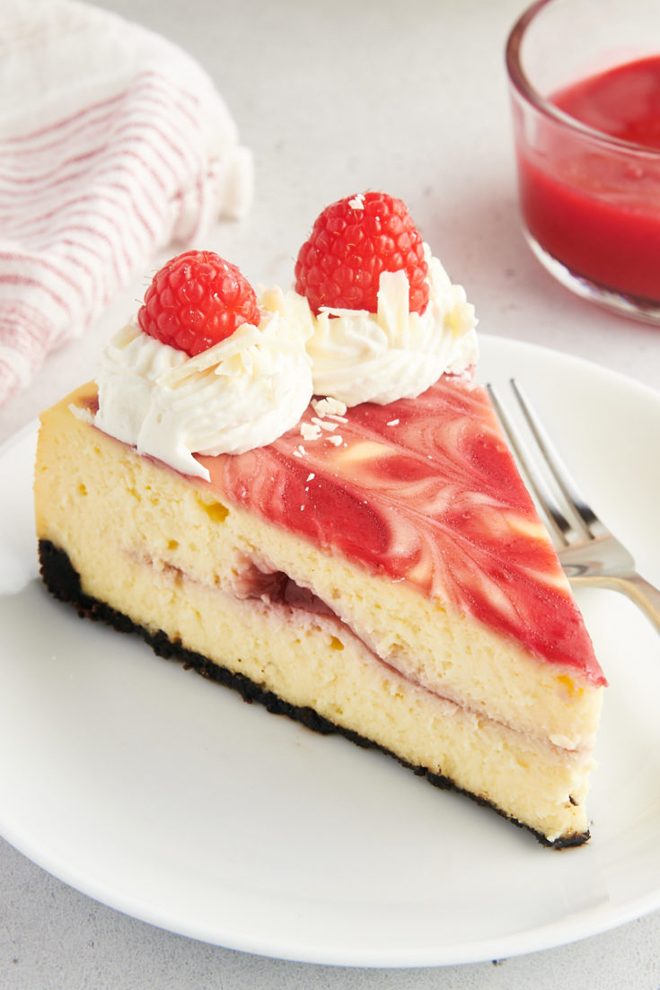 Slice of white chocolate raspberry cheesecake on white plate