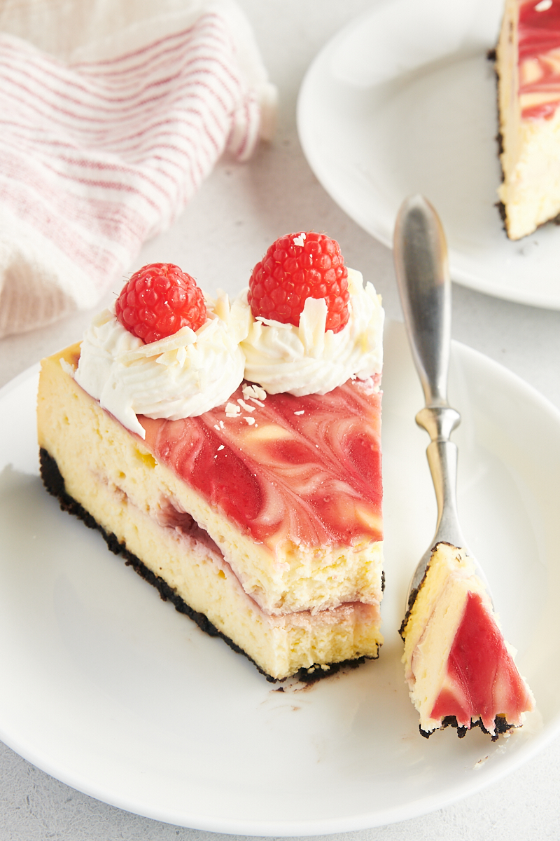 Slice of white chocolate raspberry cheesecake on plate with tip on fork