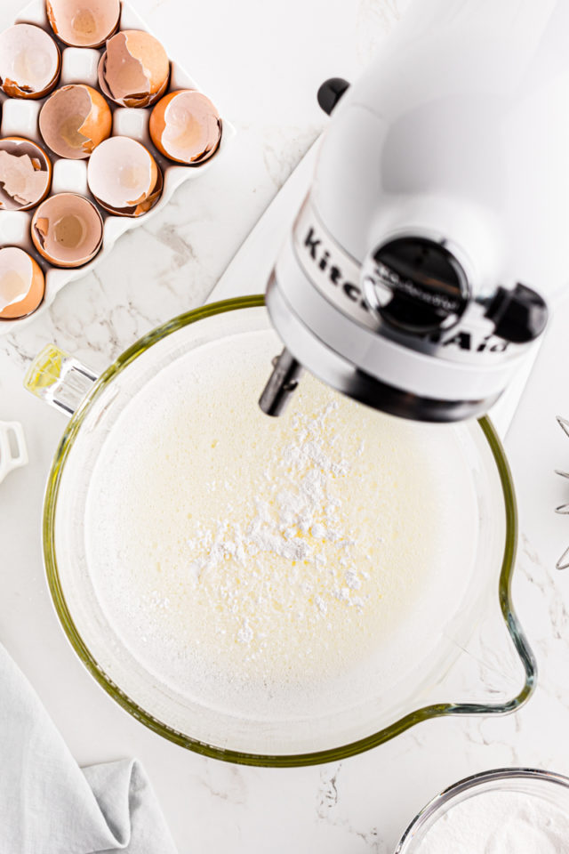 overhead view of cream of tartar and salt added to foamy egg whites in the bowl of a stand mixer