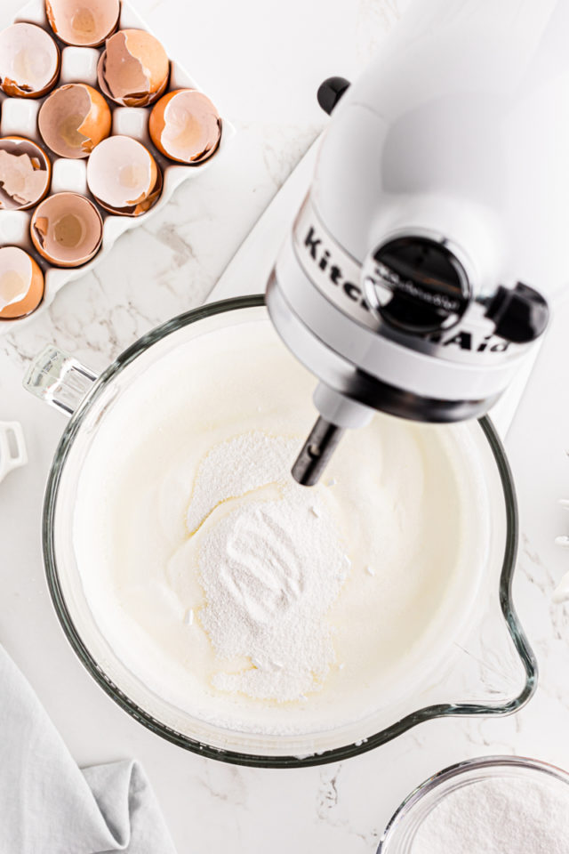 overhead view of sugar added to whipped egg whites in the bowl of a stand mixer