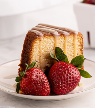 a slice of cream cheese pound cake with strawberry-white chocolate sauce and fresh strawberries on a white plate