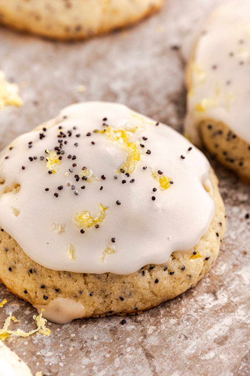 close-up of a lemon poppy seed cookie topped with lemon glaze, lemon zest, and poppy seeds