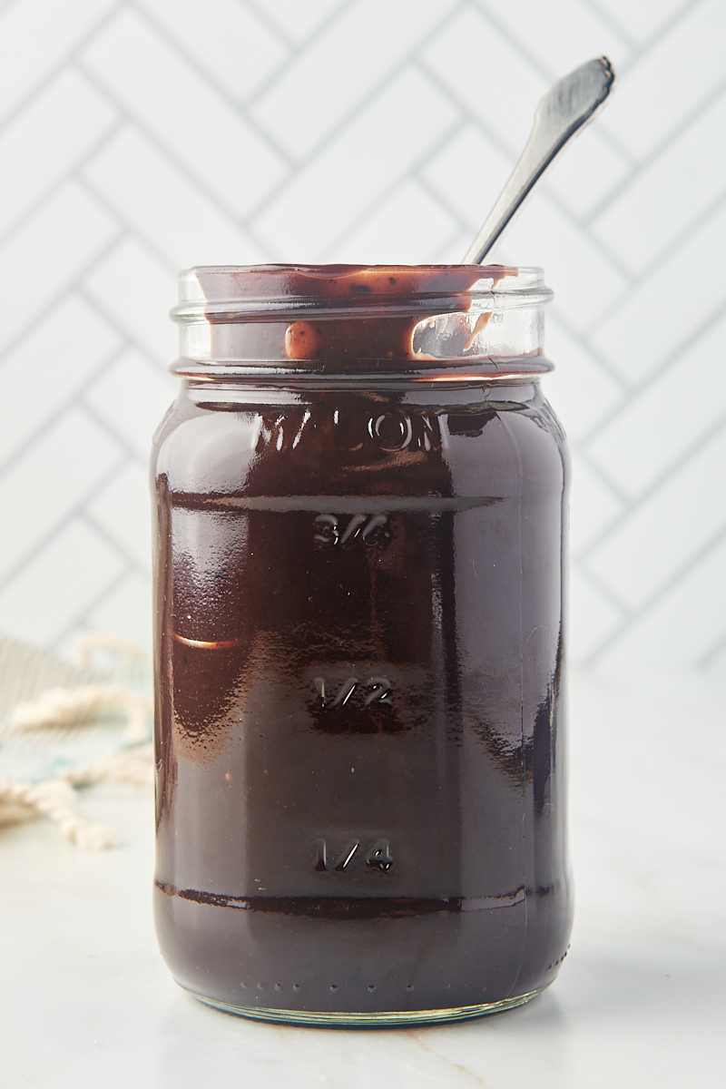 a glass jar filled with hot fudge sauce with a spoon sticking out of the top